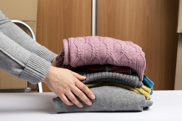Female hand holding a stack of clothes, help and volunteering concept